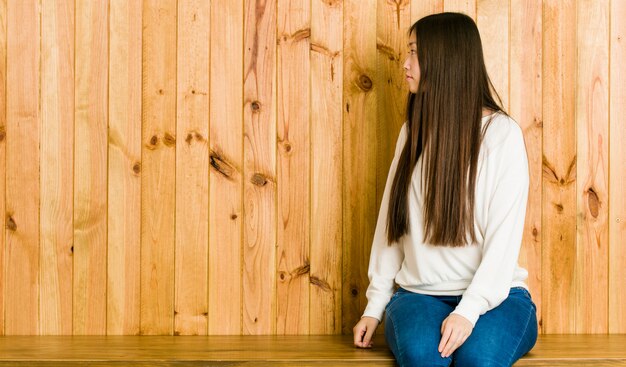 De jonge vrouwenzitting op een houten plaats die, zijdelings staren staren