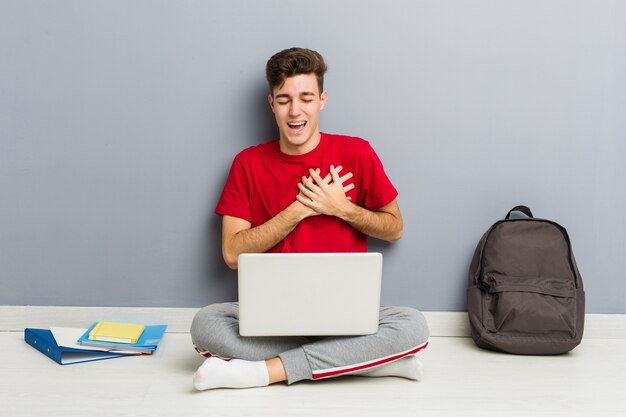 De jonge zitting van de studentenmens die op zijn huisvloer laptop houdt