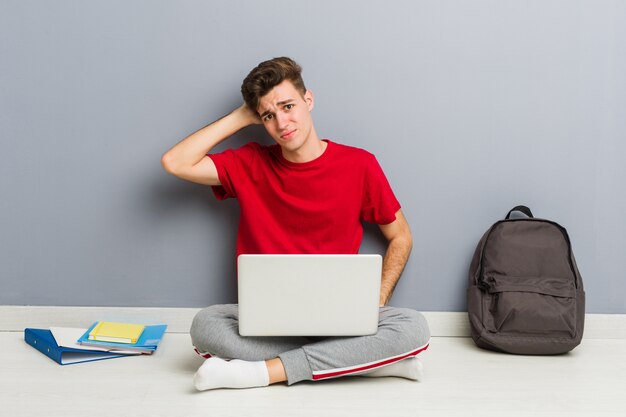 De jonge zitting van de studentenmens die op zijn huisvloer laptop houdt