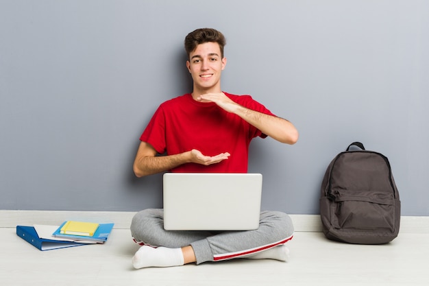 De jonge zitting van de studentenmens die op zijn huisvloer laptop houdt