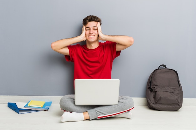 De jonge zitting van de studentenmens die op zijn huisvloer laptop houdt