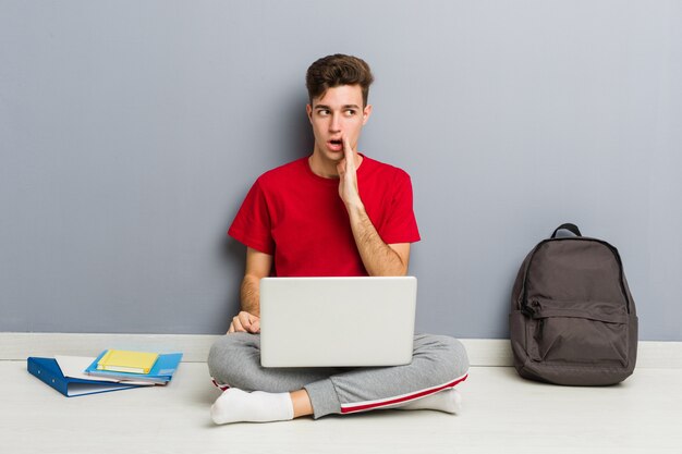 De jonge zitting van de studentenmens die op zijn huisvloer laptop houdt