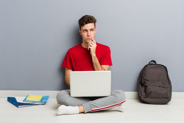 De jonge zitting van de studentenmens die op zijn huisvloer laptop houdt