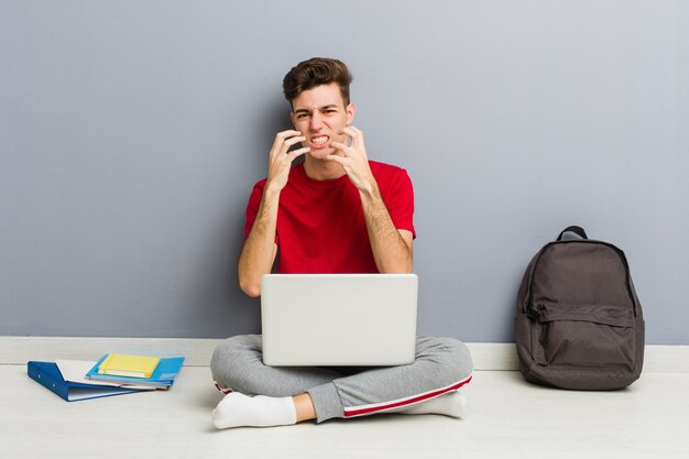 De jonge zitting van de studentenmens die op zijn huisvloer laptop houdt