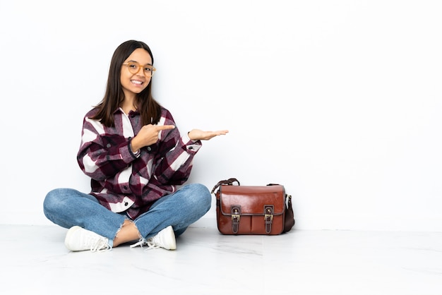 De jonge zitting van de studentenvrouw op de vloer die lege ruimte op de palm houdt om een advertentie op te nemen