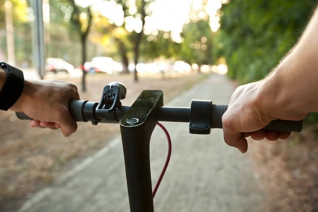 De jongeman rijdt op de elektrische scooter door de avondstad langs de paden