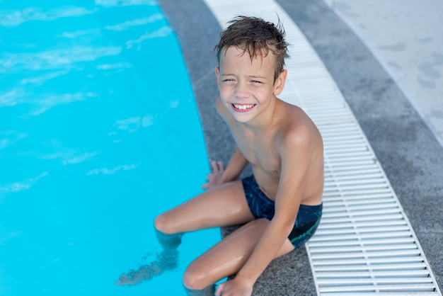 De jongen aan de kant van het zwembad lacht Het openluchtzwembad