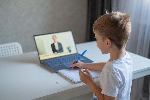 De jongen communiceert met een vrouwelijke leraar op een laptopwebcam Online les Afstandsonderwijs in quarantaine Een schooljongen studeert thuis tijdens de epidemie van het coronavirus