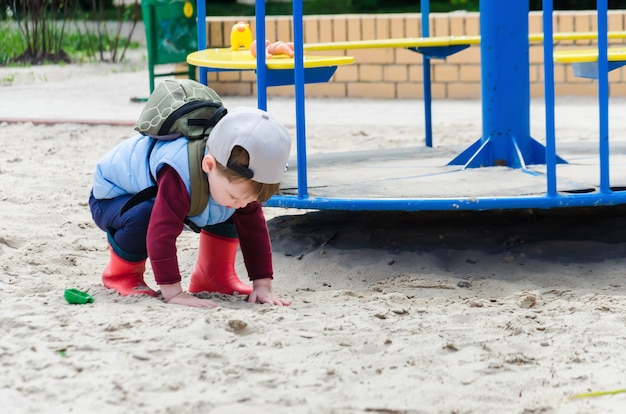 De jongen duikt in het zand bij de draaimolen van de kinderen