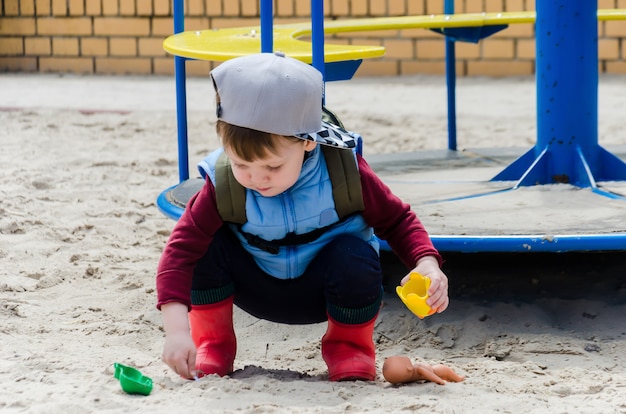 De jongen duikt in het zand bij de draaimolen van de kinderen