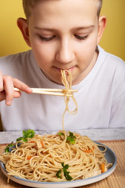 De jongen eet noedels met stokjes in het Japans met kip Portret close-up