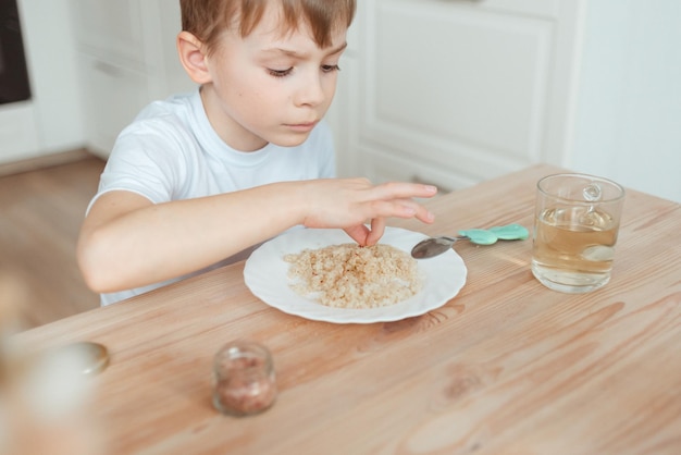 Foto de jongen eet thuis aan de eettafel in de keuken