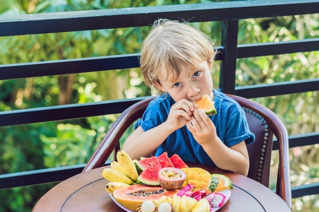 De jongen eet verschillende soorten fruit op het terras.