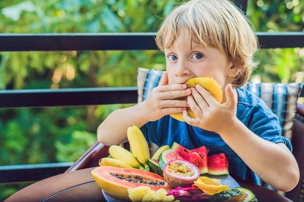 De jongen eet verschillende soorten fruit op het terras.