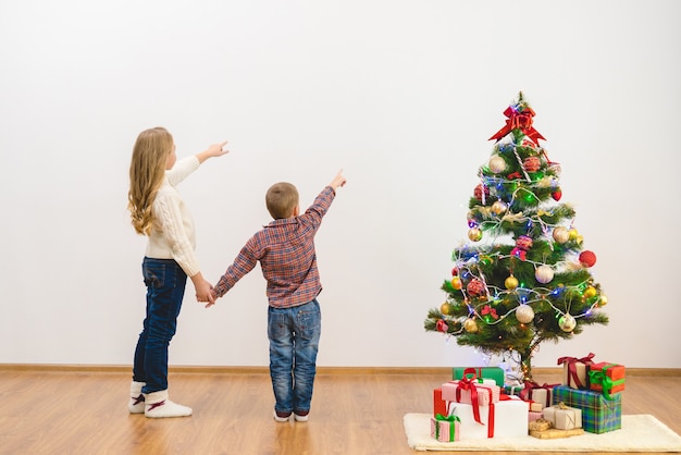 De jongen en een meisje gebaar op de witte muur bij de kerstboom