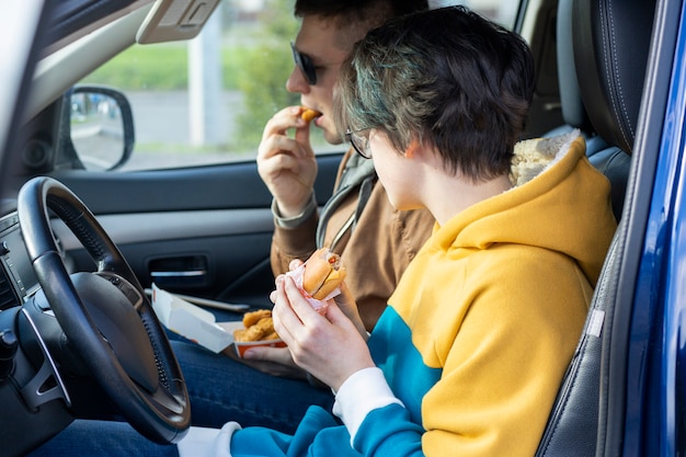 De jongen en het meisje eten fastfood in de auto zitten en praten over ongezond voedsel