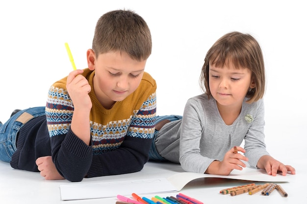 De jongen en het meisje liggen op de vloer en tekenen met potloden op een geïsoleerde witte achtergrond