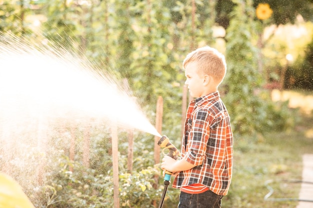 De jongen geeft het tuinbed water met een tuinslang