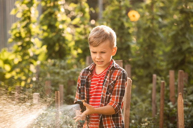 De jongen geeft het tuinbed water met een tuinslang