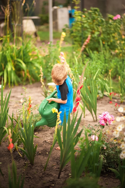 De jongen helpt met de zomertuin. Kinderspelen met water in de achtertuin.