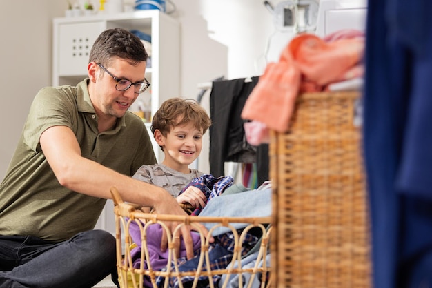 De jongen helpt zijn vader om vuile kleren in de wasmachine te doen, ze halen er dingen uit