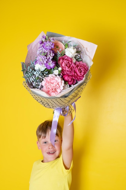 Foto de jongen houdt een bloemstuk vast in een ronde doos. een cadeau voor mama. jongen met een boeket bloemen.