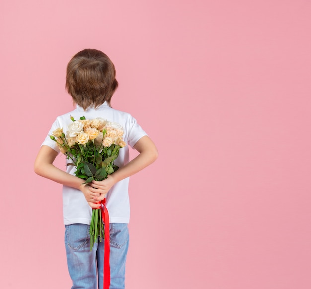 De jongen houdt een boeket bloemen achter zijn rug op een roze achtergrond. Concept van vakantie, verjaardag, Valentijnsdag en moederdag.