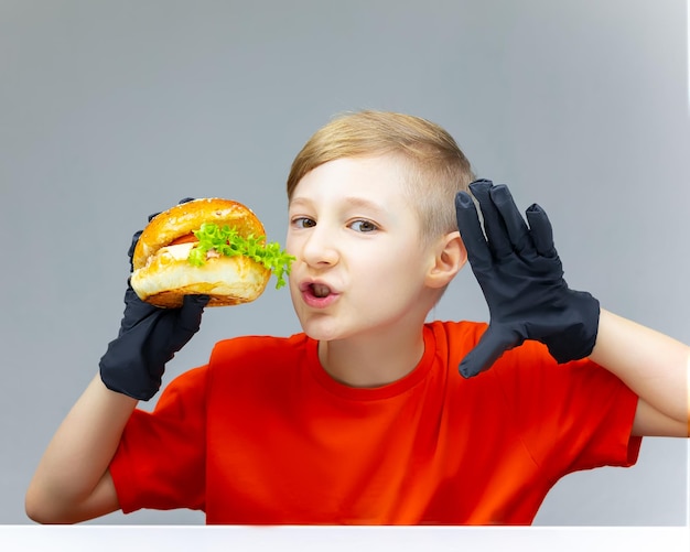 De jongen houdt een hamburger voor zich Hij heeft zwarte handschoenen aan zijn handen