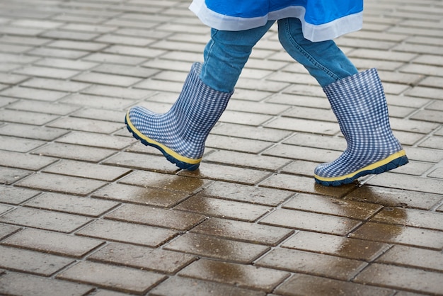 De jongen in blauwe rubberlaarzen loopt otdoor in regenachtige dag