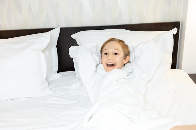 De jongen in de hotelkamer gemorst op het bed in een witte jas gooide het over zijn hoofd en lacht vrolijk