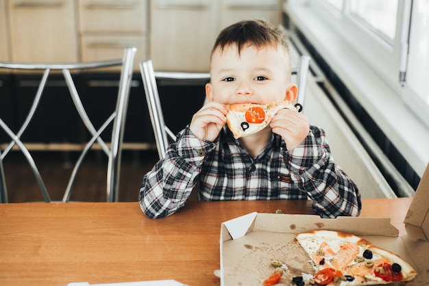 De jongen in de keuken die thuis pizza met zalm eet