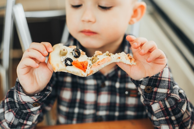 De jongen in de keuken die thuis pizza met zalm eet