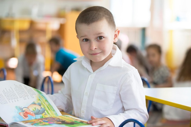 De jongen is een kleuter Portret van een zesjarig kind met een boek Junior student aan een bureau