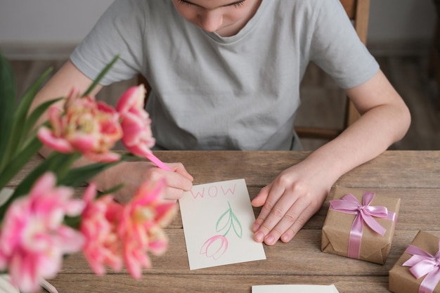 De jongen maakt een kaart voor moederdag Kindertekeningen