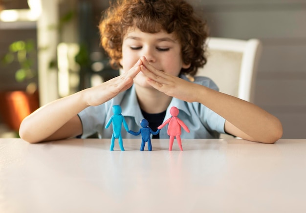 de jongen maakte plasticine figuren van mama papa en kind en vouwde zijn handen huis erover