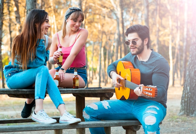 De jongen met meisjes speelt gitaar en zingt in openlucht, partij