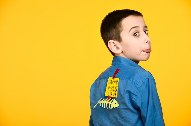 De jongen op een gele achtergrond in een blauw shirt met een vis gelijmd tape en een stuk papier op zijn rug