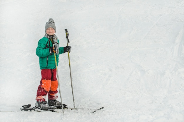 De jongen op ski's met skistokken glimlacht.