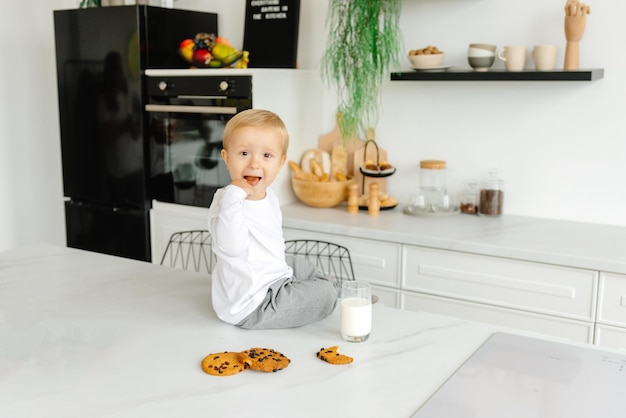 De jongen slakken en houdt een havermoutkoekje met melk in zijn handen in het keukenontbijt in de mo