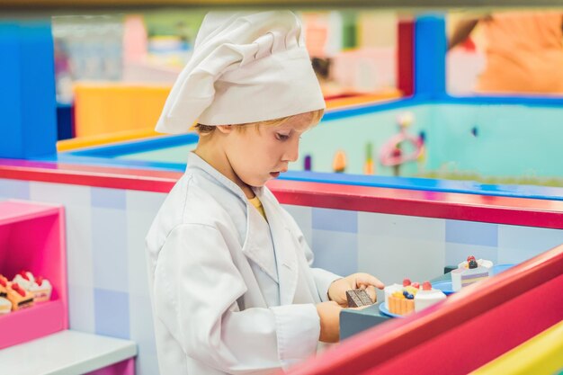 De jongen speelt het spel alsof hij een kok of een bakker is in een kinderkeuken