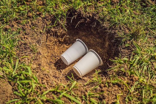 De jongen speelt recycling, hij begraaft plastic wegwerpschalen en biologisch afbreekbare borden