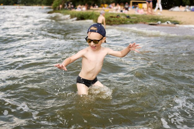 De jongen staat in het water met een pet en zonnebril op