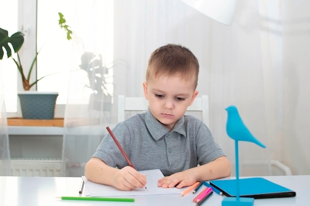 De jongen tekent in zijn kamer aan zijn bureau Het kind is thuis bezig met creativiteit Het concept van de creativiteit van kinderen Selectieve focus