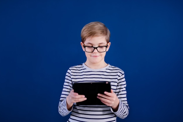 De jongen van het blondekind die met grote glazen met tabletpc spelen op blauwe muur. Onderwijs concept.