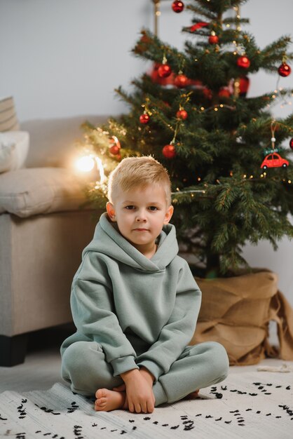 De jongen zit in de buurt van de kerstboom met geschenken. Kinderen voor de kerstvakantie.