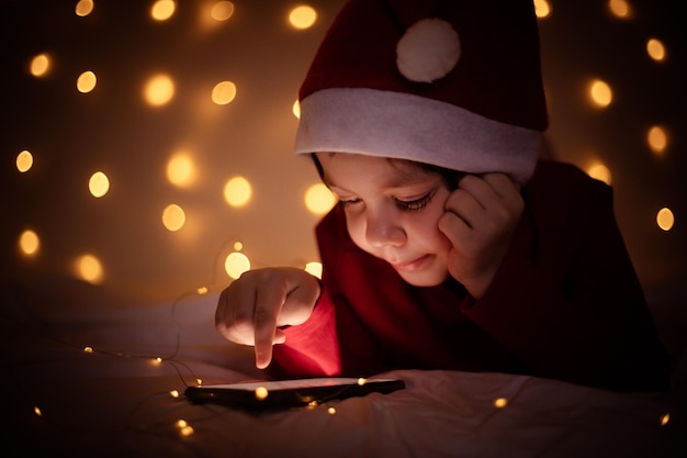De jongen zit in de telefoon op de achtergrond van een slinger Nieuwjaar en Kerstmis Feestelijke stemming