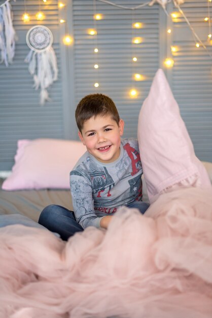 De jongen zittend op het bed en roze kussen in zijn handen te houden in de kerstkamer