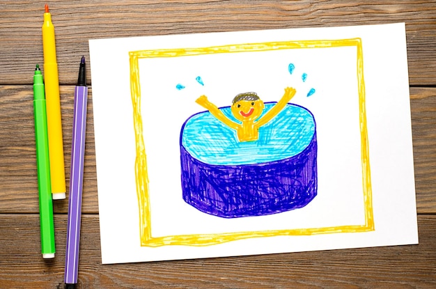 De jongen zwemt vrolijk in het zwembad Kindertekening op papier Houten tafel met stiften