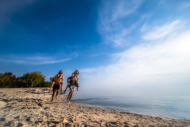 De jongens dragen meisjes op hun schouders en rennen op het strand