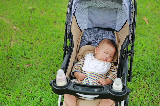 De jongensslaap van de close-up Aziatische pasgeboren baby in wandelwagen op aardpark.